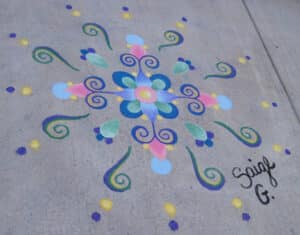 Sidewalk chalk drawing with swirls and dots of blue pink yellow