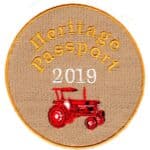 Beige circular cloth patch with Heritage Passport embroidered in gold letters 2019 in white and red tractor