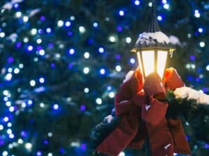 Snow dusted old-fashioned black Lamppost with red bow and background of many tiny blue and white lights