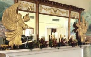 two gold angels and evergreen garland on white mantel with mirror above