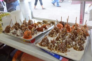 Two trays of brown and white chocolate and red candy apples on white counter inside booth by window