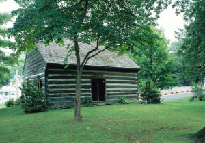 Green lawn with gray and white log Quaker meetinghouse built 1789 large tree shading it