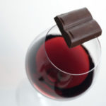 glass of red wine with two squares of chocolate balanced on top