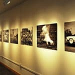 Five black and white photographs displayed in a row on cream wall under track lighting