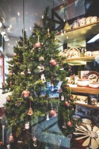 view through glass to Christmas tree with red ornaments and wood store shelves with pottery and wooden gifts