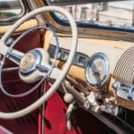 Closeup - beige and silver metal steering wheel and dashboard in antique car with red interior