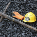 Coal miner's pick, orange glove, yellow hardhat with lamp lying on bed of black coal
