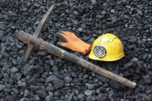 Coal miner's pick, orange glove, yellow hardhat with lamp lying on bed of coal