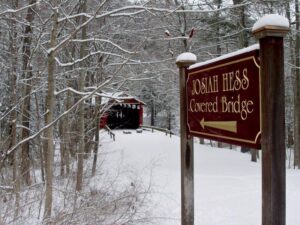 Sign for Josiah hes Covered Bridge in foreground, snow covered trees and bridge in background