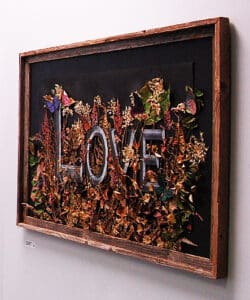 wooden framed art work with word L O V E against dark background with flowers