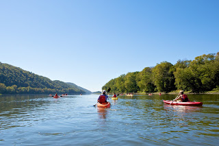 two red kayaks paddling away down river, other yellow, red kayaks in distance, blue sky overhead