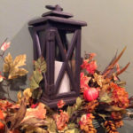 Orange and red all leaves surrounding bronze lantern with white pillar candle