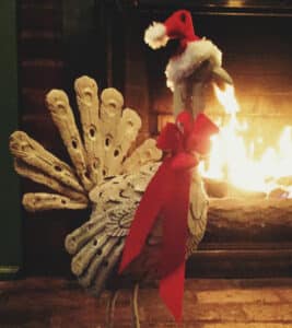 Turkey sculpture with red bow around neck and Santa hat in front of blazing fireplace