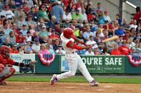 baseball player in white uniform with red sleeves and helmet hitting baseball with fans in stands behind Danville!