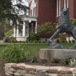 bronze statue of Husky in front of red brick campus building with white columns on portico