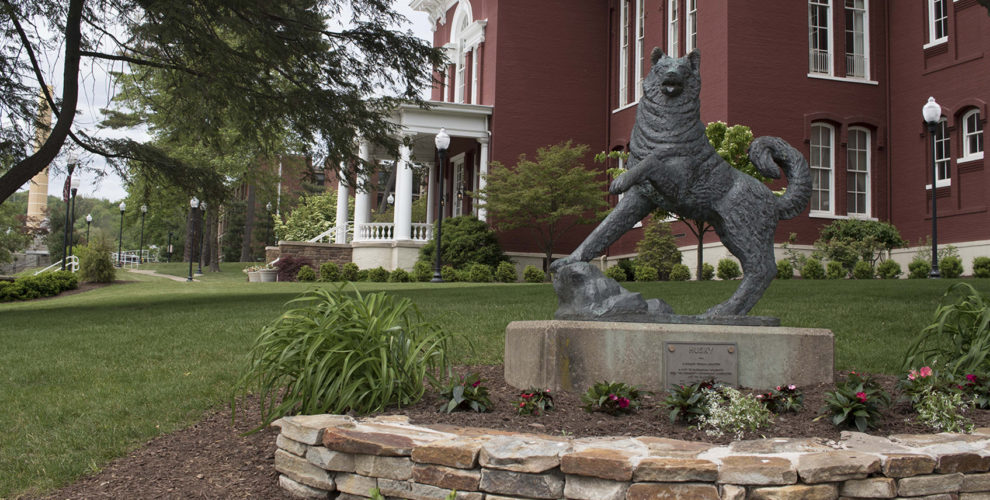 bronze statue of Husky in front of red brick campus building with white columns on portico