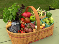 oval woven wicker basket with handle, red trim holding lettuce, tomatoes, eggs, etc. on green wooden plank table