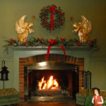 red brick fireplace with green mantel and wall Christmas wreath above with red bow 2 gold angels on mantel