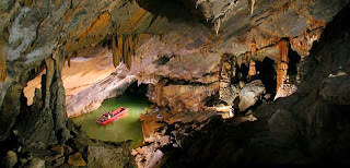 underground cavern with gray and brown stalactites and stalagmites surrounding green pool with red boat