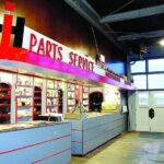 International Harvester prototype dealership interior – shelves of tools behind gray service counter with red horizontal stripes, red overhang, IH Parts Service sign above