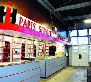  International Harvester prototype dealership interior – shelves of tools behind gray service counter with red horizontal stripes, red overhang, IH Parts Service sign above 