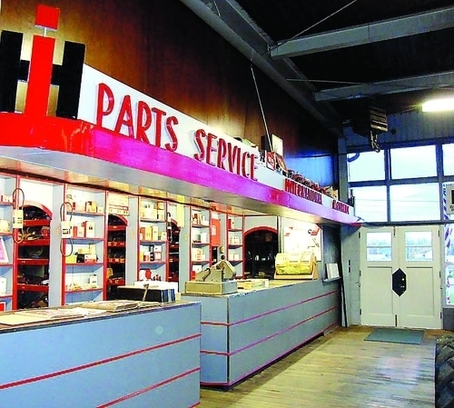 International Harvester prototype dealership interior – shelves of tools behind gray service counter with red horizontal stripes, red overhang, IH Parts Service sign above