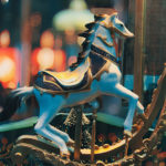 Antique blue carousel horse with gold rockers and black mane and tail with out-of-focus carousel in background