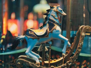 Antique blue carousel horse with gold rockers and black mane and tail with out-of-focus carousel in background