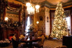 Victorian drawing room at Christmas with tree, table and chairs in front of fireplace decorated with greens