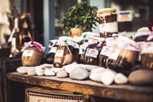 homemade jam in jars with cloth covered tops behind rounded grey stones displayed on rustic brown table