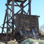 brown wooden mine shaft entrance and superstructure on rocky ground, blue sky behind