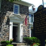 2 story PA stone house, white windows and doorway moldings, American flag mounted on doorway, Montgomery House historic street sign