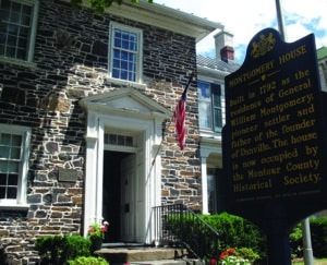 2 story PA stone house, white windows and doorway moldings, American flag mounted on doorway, Montgomery House historic street sign