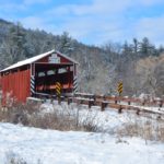 Kramer Covered Bridge - snow covered red bridge with brown wood guardrails on either side of road leading to bridge