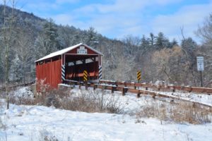 Kramer Covered Bridge - snow covered red bridge with brown wood guardrails on either side of road leading to bridge
