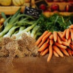 piles of fresh leeks and carrots with green tops on brown wood table with wood crates in background