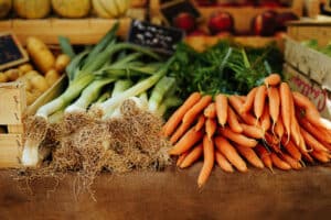 piles of fresh leeks and carrots with green tops on brown wood table with wood crates in background