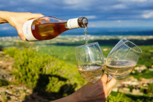 hand holding wine bottle pouring wine into two glasses against background landscape