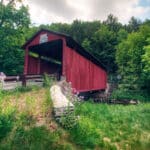 Sam Eckman Covered Bridge - approach to red covered bridge with green grassy area in front and trees behind