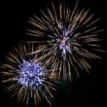 Two sunburst fireworks with blue white centers and gold streamers against night sky