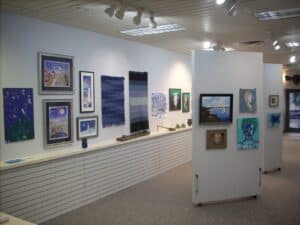 art gallery hung with blue paintings on white walls with greybrown carpet