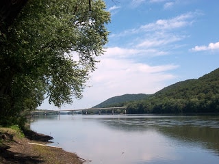 view along side the Susquehanna River with mountains of trees on the side and bridge over passing in the distance