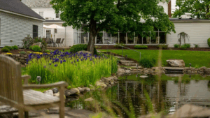exterior garden of the inn with a pond surrounded by purple flowers stone paths and outdoor seating under a tree 