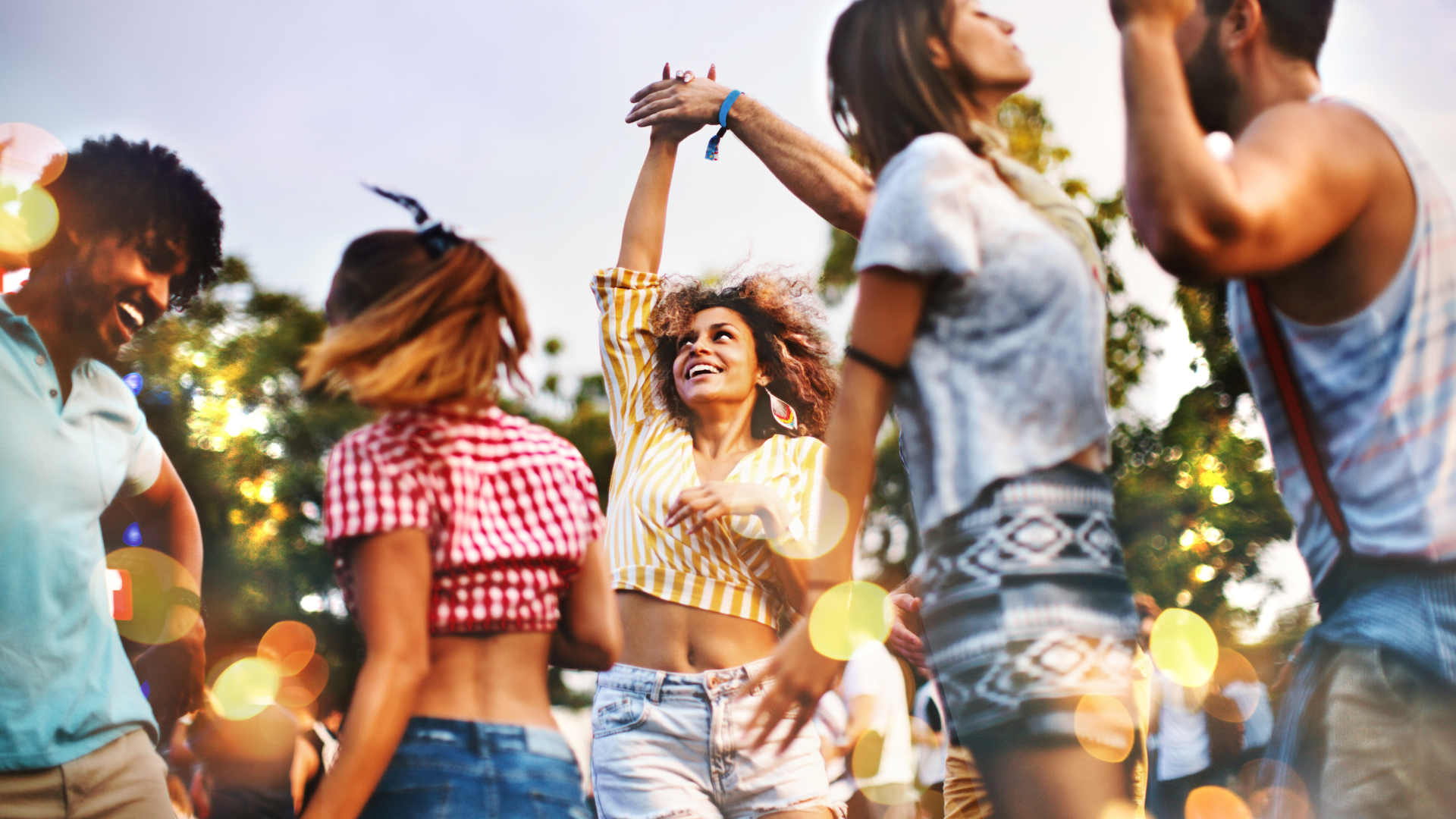 people dancing at an outdoor summer concert surrounded by warm lights and trees