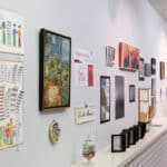 Over 20 art works in different media hanging on white wall