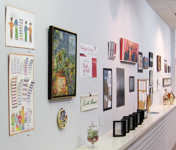 Over 20 art works in different media hanging on white wall