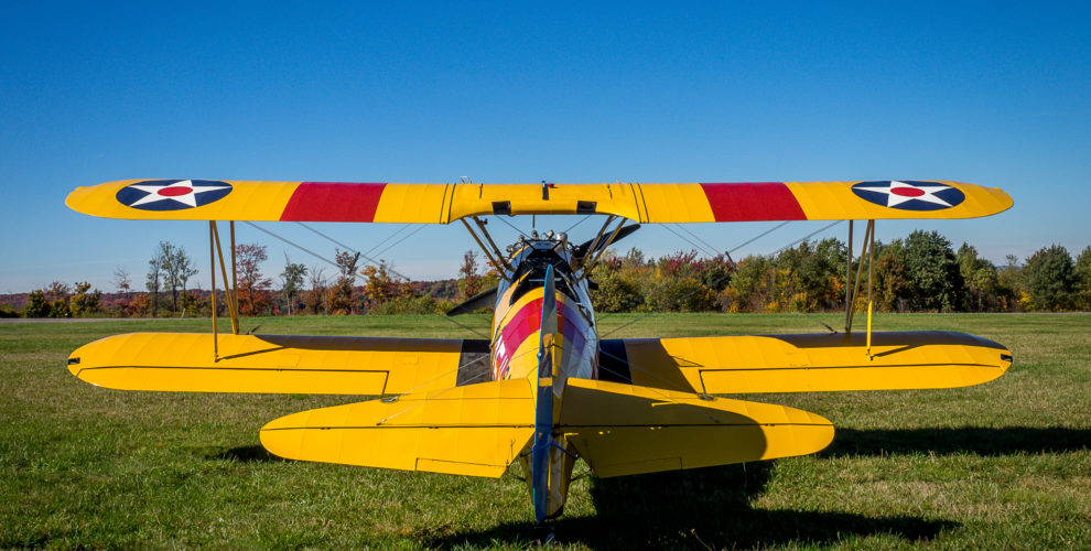 Vintage Steerman yellow bi-plane with red & yellow striped wings on grassy airfield