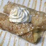 apple filled crepes drizzled with maple glaze & confectioners sugar on white plate