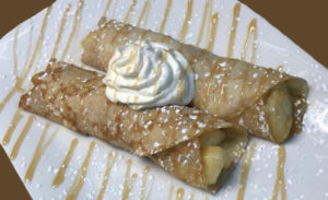 apple filled crepes drizzled with maple glaze & confectioners sugar on white plate