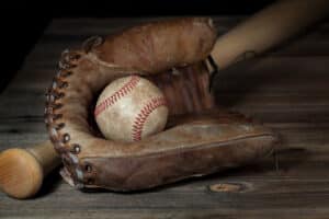 Dirty baseball nested in brown baseball glove lying against bat at angle behind on wooden surface